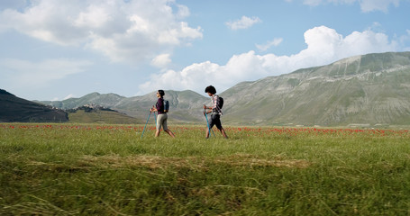 Aerial view flying above two people couple hiking or nordic walking outdoor on a trail path near flower fields in Castelluccio di Norcia. side follow. Friends italian trip in Umbria.4k drone