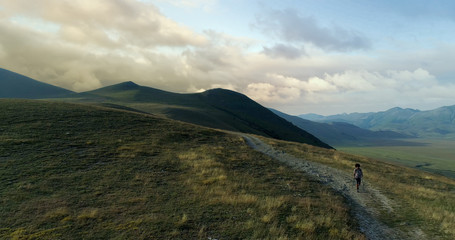 Aerial view flying above hiker man hiking or nordic walking outdoor on a trail path near Castelluccio di Norcia at sunset or sunrise.Approaching forward. Friends italian trip in Umbria.4k drone