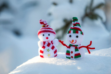 Two small funny toys baby snowman in knitted hats and scarves in deep snow outdoors on bright blue and white copy space background. Happy New Year and Merry Christmas greeting card.