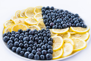 Blueberry berries and lemon slices on a round plate on a white background. Top angle view....