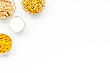 Various cereals in bowls and milk on white background top view copyspace