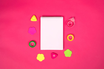 White notebook with different school  colorful supplies on pink background. Back to school