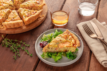 A slice of French quiche with salmon, with green salad leaves, thyme and white wine, on a dark...