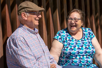 Pareja de gente mayor (abuelos) sentados en un banco descansando del paseo. Se ríen y hablan entre...