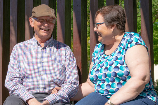 Pareja de gente mayor (abuelos) sentados en un banco descansando del paseo. Se r&iacute;en y hablan entre ellos.