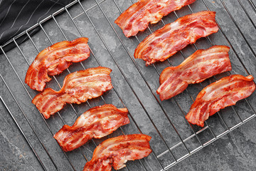 Cooling rack with tasty fried bacon on grey background