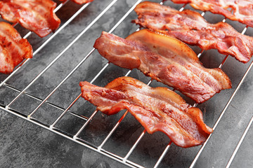 Cooling rack with tasty fried bacon on grey background