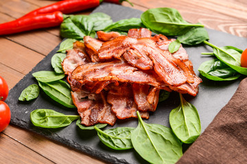 Slate plate with fried bacon on wooden table