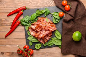 Slate plate with fried bacon on wooden table