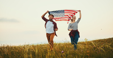 happy couple man and woman with flag of united states enjoying the sunset on nature