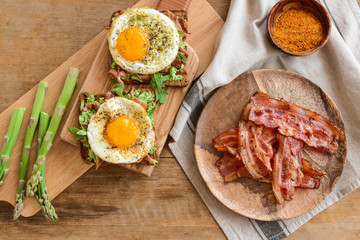 Tasty toasts with bacon and fried egg on wooden background