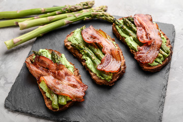 Tasty toasts with bacon on slate plate