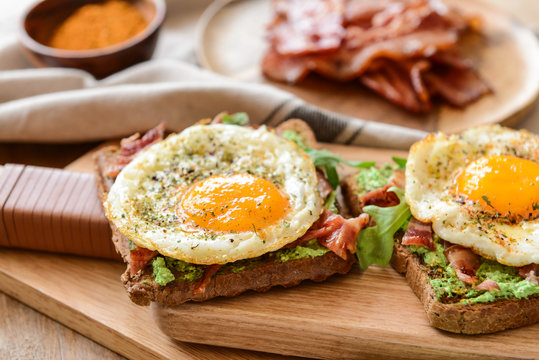 Tasty toasts with bacon and fried egg on wooden board