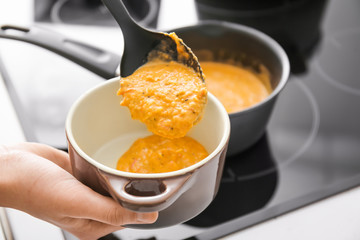 Woman pouring delicious cream soup into pot, closeup