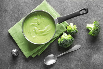 Saucepan with delicious broccoli cream soup on grey background