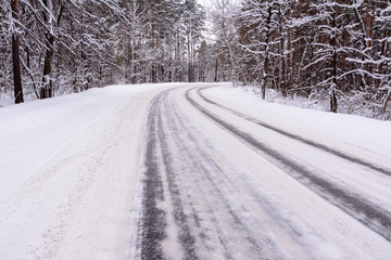 Fototapeta premium Patterns on the winter highway in the form of four straight lines. Snowy road on the background of snow-covered forest. Winter landscape.