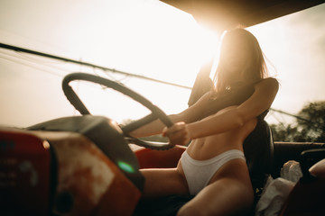 A woman is driving a tractor in a white bikini on the farm.