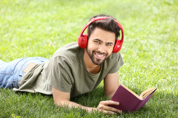 Young man listening to music and reading book in park