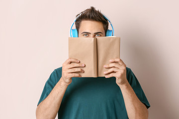 Young man listening to music and reading book on light background