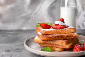 Plate with tasty French toasts and strawberry on grey table