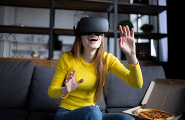 Beautiful woman touching air during the VR experience. Girl eats pizza