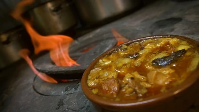 Bubbling, hearty Spanish comfort food (beef tripe stew) cooked over coal stove, filmed in slow motion.