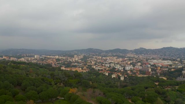 Aerial drone shot, over a forest and park, overlooking trees and buildings in the city of Cannes, on a cloudy day, in the French Riviera, in France at La Croix des gardes