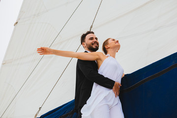 Handsome man hugging attractive woman outstretching hands wide on yacht in bright day