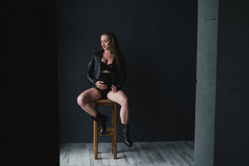 Pregnant caucasian long-haired woman wearing black leather jacket, lingerie and boots. Pregnancy, happiness, expectation concept.