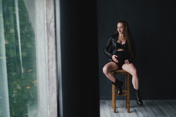 Pregnant caucasian long-haired woman wearing black leather jacket, lingerie and boots. Pregnancy, happiness, expectation concept.