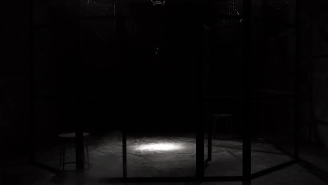 White smoke Projection in a metal grilles cage, circular MMA boxing ring, in a dark studio with a Spotlight or light shower. Show with Vintage microphone. Tracking in. 4K. White dust on the ground.
