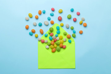 Green envelope and multi-colored candies on a bright trendy light blue background. top view