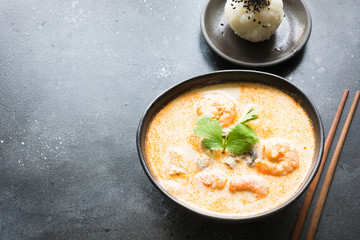 Tom yam kung spicy thai soup with shrimp, seafood, coconut milk, chili pepper and rice in black bowl. Close up. Asian food.