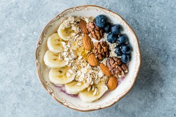 Acai Bowl with Yogurt, Blackberry, Banana Slices, Walnut, Honey, Jam, Oat, Almond, Sesame Seeds and Granola in Porcelain Bowl.