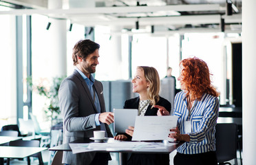 A group of young business people with tablet sitting in an office, talking.