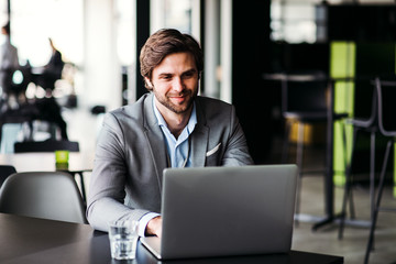 A portrait of young businessman with computer in an office, looking at camera.