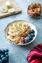 Acai Bowl with Yogurt, Blackberry, Banana Slices, Walnut, Honey, Jam, Oat, Almond, Sesame Seeds and Granola in Porcelain Bowl.