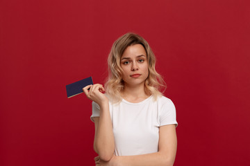 Portrait of a beautiful girl with curly blond hair dressed in a white t-shirt standing on a red background.