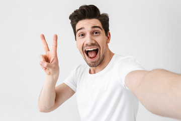 Excited happy young man posing isolated over white wall background make a selfie by camera.