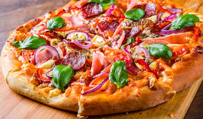Pizza with Mozzarella cheese, ham, tomato sauce, salami, onion, pepper, Spices and Fresh basil. Italian pizza on wooden table background