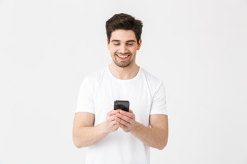 Fototapeta na wymiar Excited happy young man posing isolated over white wall background using mobile phone.