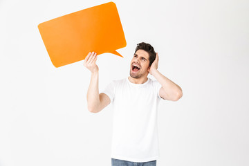 Emotional screaming young man posing isolated over white wall background holding speech bubble.