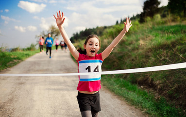 Small girl runner crossing finish line in a race competition in nature.