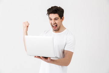 Happy excited young man posing isolated over white wall using laptop computer make winner gesture.