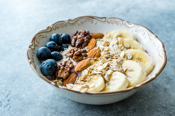 Acai Bowl with Yogurt, Blackberry, Banana Slices, Walnut, Honey, Jam, Oat, Almond, Sesame Seeds and Granola in Porcelain Bowl.