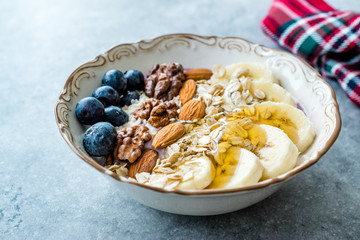 Acai Bowl with Yogurt, Blackberry, Banana Slices, Walnut, Honey, Jam, Oat, Almond, Sesame Seeds and Granola in Porcelain Bowl.