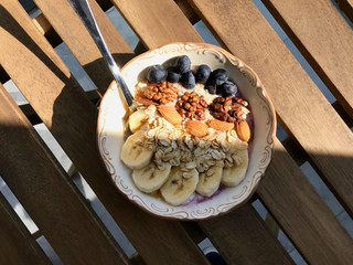 Acai Bowl with Yogurt, Blackberry, Banana Slices, Walnut, Honey, Jam, Oat, Almond, Sesame Seeds and Granola in Porcelain Bowl.