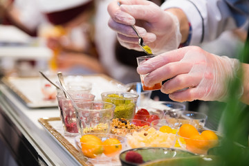 Chef wearing white gloves and standing behind full lunch service station with assortment of food