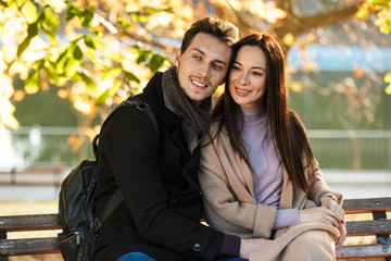 Happy young beautiful loving couple posing walking outdoors in park nature sitting on bench.