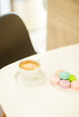 Cup of coffee and testy macaroons on white table in cafe.